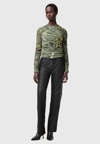 Gerippter grüner Langarmoberteil mit floralem Muster, kombiniert mit schwarzen Leder-Hosen im Straight-Leg-Stil und spitzen schwarzen Absätzen.