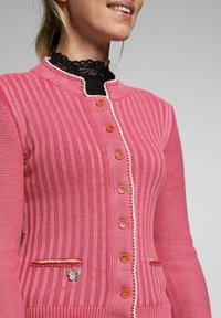 Rosa gerippter Cardigan mit Rundhalsausschnitt, orangefarbenen Knöpfen, weißen Akzenten und einem dekorativen Schmetterling auf einer Tasche.