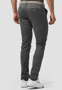 Pantalones gris ajustados con un acabado de tela suave, que cuentan con bolsillos traseros con botones y una cinturilla con estampado. Llevados con zapatillas blancas.