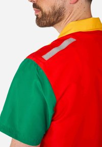 Košulja kratkih rukava s crvenim prednjim dijelom, zelenim rukavima i žutim ovratnikom. Uključuje reflektirajući sivi detalj na ramenu.