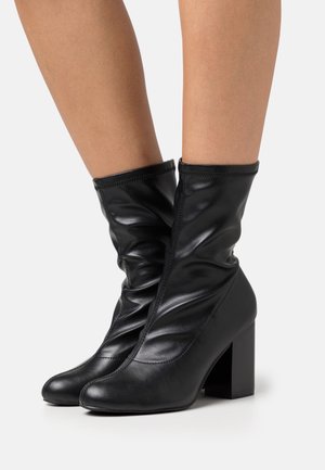 Botas de cuero negro hasta el tobillo con un diseño arrugado, puntas redondeadas y tacón cuadrado. Textura suave con detalles de costura.