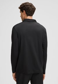 Czarna koszulka polo z długim rękawem, uszyta z gładkiego materiału, z klasycznym kołnierzykiem i luźnym krojem. Prosty, nieozdobiony design.