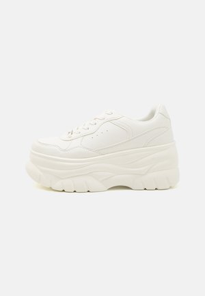 Biały masywny sneaker na platformie z sznurowaniem i grubą teksturowaną podeszwą na jasnym tle.