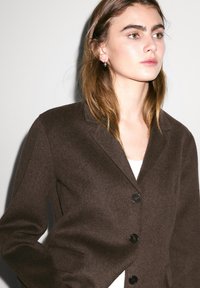 Brown wool blend blazer with a notched collar, single-button closure, and textured fabric. Features black buttons and tailored fit.