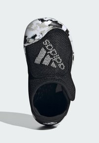 Scarpa in mesh nera con suola a motivo camouflage, cinturino elastico e dettagli bianchi del logo. Design aperto che espone l'interno.