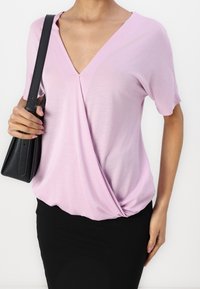 Roze V-hals top met korte mouwen, met een gedraaide detail bij de taille. Gecombineerd met een zwarte aansluitende rok en een zwarte handtas.