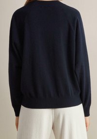 Mörkblå stickad tröja med ribbad halsringning och fåll, som har en lös passform och långa raglanärmar. Mjuk textur, minimal design.