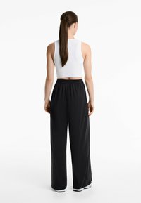 Vit ärmlös crop top kombinerad med svarta, löst sittande byxor med elastisk midja. Släta texturer med en avslappnad siluett.