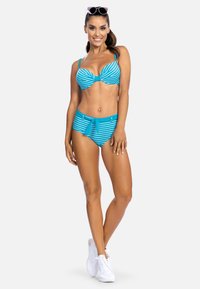 Bikini w paski w kolorze teal i białym, z węzełkiem z przodu, wysokim stanem i gładką fakturą. Noszony z białymi trampkami.
