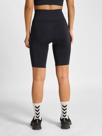 Widok z tyłu osoby noszącej czarne szorty rowerowe z wysokim stanem, białe skarpetki za kostkę z czarnymi szewronami oraz czarne buty sportowe.