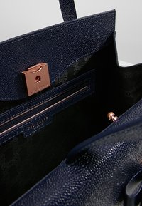 Granatowa skórzana torebka o fakturowanym wykończeniu, z różowozłotymi akcentami, magnetycznym zapięciem oraz zapinaną na zamek wewnętrzną kieszenią.