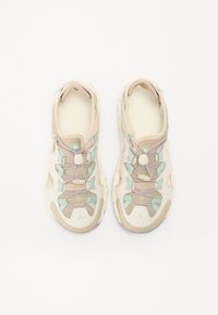 Sneakers with a cream mesh upper, beige accents, and mint green lacing. Features a textured exterior and a padded collar for comfort.