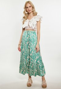 Fehér cropped top fodros ujjakkal, hosszú zöld paisley mintás szoknyával párosítva. A modellen szíjas szandál van.