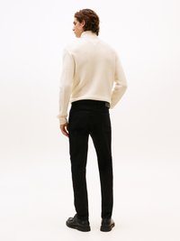 Suéter de punto color crema con un cuello alto, con detalles texturizados en los lados. Combinado con pantalones negros ajustados y zapatos negros.