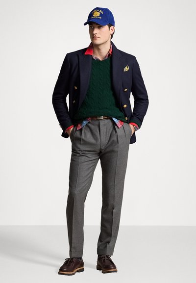 Ναυτικό μπλέιζερ με χρυσά κουμπιά, πράσινο στυλ καλωδίου πουλόβερ, καρό πουκάμισο, γκρίζες παντελόνα, μπλε καπέλο με κίτρινο κείμενο, καφέ παπούτσια.
