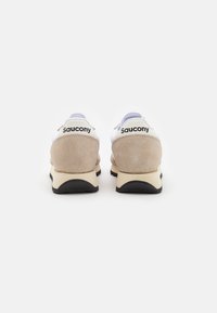 Sneakers Saucony con tomaia bianca, tallone in suede beige e suola nera. Il nome del marchio è ben visibile sul retro.