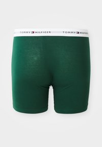 Dunkelgrüne Herren-Boxershorts mit weißem Elastikbund, der das Tommy Hilfiger-Logo und ein Flaggenmuster zeigt.