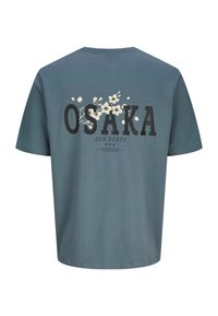 T-shirt in cotone verde con testo nero "OSAKA" e "OUR ROOTS", con design floreale bianco sopra. Maniche corte e collo tondo.