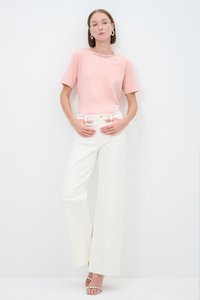 Light pink short-sleeve t-shirt with a beaded neckline, paired with high-waisted, wide-legged white trousers, and silver strappy sandals.