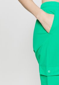 Zielone spodnie cargo z elastycznym pasem, boczną kieszenią i guzikami przy nogawce. Gładki, lekki materiał o swobodnym kroju.
