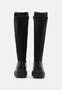 Bottes noires à hauteur de genou avec un dessus lisse et extensible et un talon en cuir texturé. Elles disposent d'une semelle en caoutchouc noir et de zips sur les côtés.