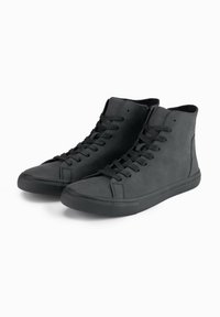 Zapatillas altas negras de cuero texturizado, con puntera redonda, suela plana de goma y cordones estándar en la parte delantera. Diseño minimalista.