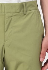 Pantalones verde claro hechos de una tela suave y ligera. Incluyen bolsillos laterales, pasadores para cinturón y detalles de costura visibles.