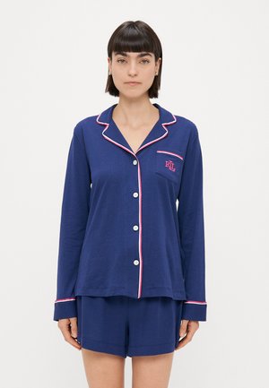 Námornícky modrá súprava pyžama s košeľou na gombíky, ktorá má biele a ružové lemovanie, a zodpovedajúce šortky. Obsahuje malú náprsné vrecko s logom.