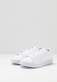Vita sneakers med en slät läderovandel, texturerad gummisula och rund tå. Har platta snören och en diskret logotyp på sidan.