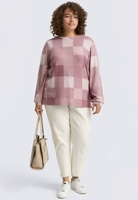 Pull léger texturé à carreaux rose et crème, associé à un pantalon crème et des baskets blanches. Le mannequin porte un sac beige.