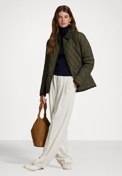 Green quilted jacket with button closures, navy turtleneck, white wide-leg pants, and brown bag. Features a classic collar and pockets.