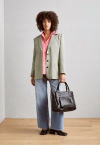 Světlý zelený blejzr s vzorem houndstooth, růžová košile na knoflíky, světle modré džíny s širokými nohavicemi, černá kožená kabelka, hnědé boty na podpatku, stylizované s přirozenými kudrlinami.