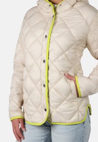 Giacca trapuntata color crema con cappuccio, rifiniture in neon verde a contrasto e bottoni a pressione, dotata di tasche laterali e una texture morbida e liscia.
