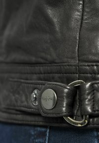 Zwarte leren jack met textuurstof, contrasterende stiksels en een metalen knoopsluiting met een gegraveerd logo detail.