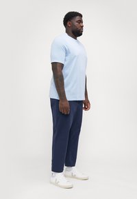 Lys blå kortermet skjorte med avslappet passform, sammen med mørk marineblå bukser og hvite joggesko med grå detaljer.