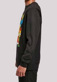 Hombre vestido con sudadera negra con personajes de dibujos animados coloridos disfrazados de Santa y elfos en la parte delantera, de perfil.