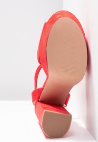 Chaussure à talon haut en cuir suédé rouge avec une tige texturée, une large bride, et une semelle solide beige. Le talon a un design en bloc pour plus de stabilité.
