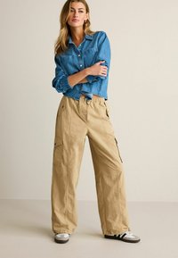 Blå denim skjorte med knaplukning, to brystlommer, parret med beige cargo bukser med sidelommer og elastisk talje.