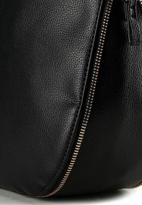 Zwarte lederen tas met een gestructureerd oppervlak, een opvallende ritssluiting met goudkleurige details en een afgeronde vorm.