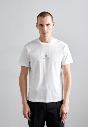 Camiseta de algodón blanca con cuello redondo que presenta un dibujo de líneas negras minimalista de manos formando un corazón en la parte frontal.