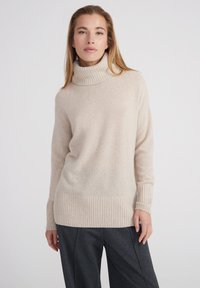 Pull à col roulé beige en matière douce avec ourlet côtelé et poignets de manches, présentant une coupe décontractée et un design minimaliste.