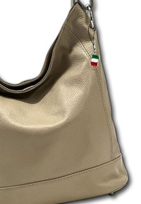 Sac en cuir beige à bandoulière avec une finition texturée, comportant un petit charme en forme de drapeau italien attaché à une sangle en métal.
