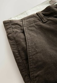 Dunkelbraune Cordhosen mit sichtbaren Nähten, einem Gürtelschlaufe, einer Vordertasche und einem weißen Futter am Bund.