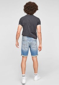 Vaaleansiniset farkkushortsit, joissa on käännetyt lahkeet, ovat yhdistetty tummansinisään T-paitaan, jossa on valkoisia yksityiskohtia. Asusteena ovat valkoiset lenkkarit.