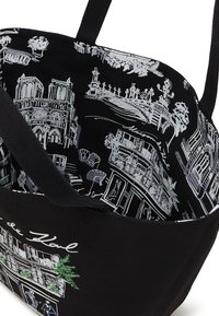 Sac en tissu noir avec des dessins en ligne blanche de bâtiments et d'arbres à l'intérieur, featuring un accent vert et de solides poignées noires.