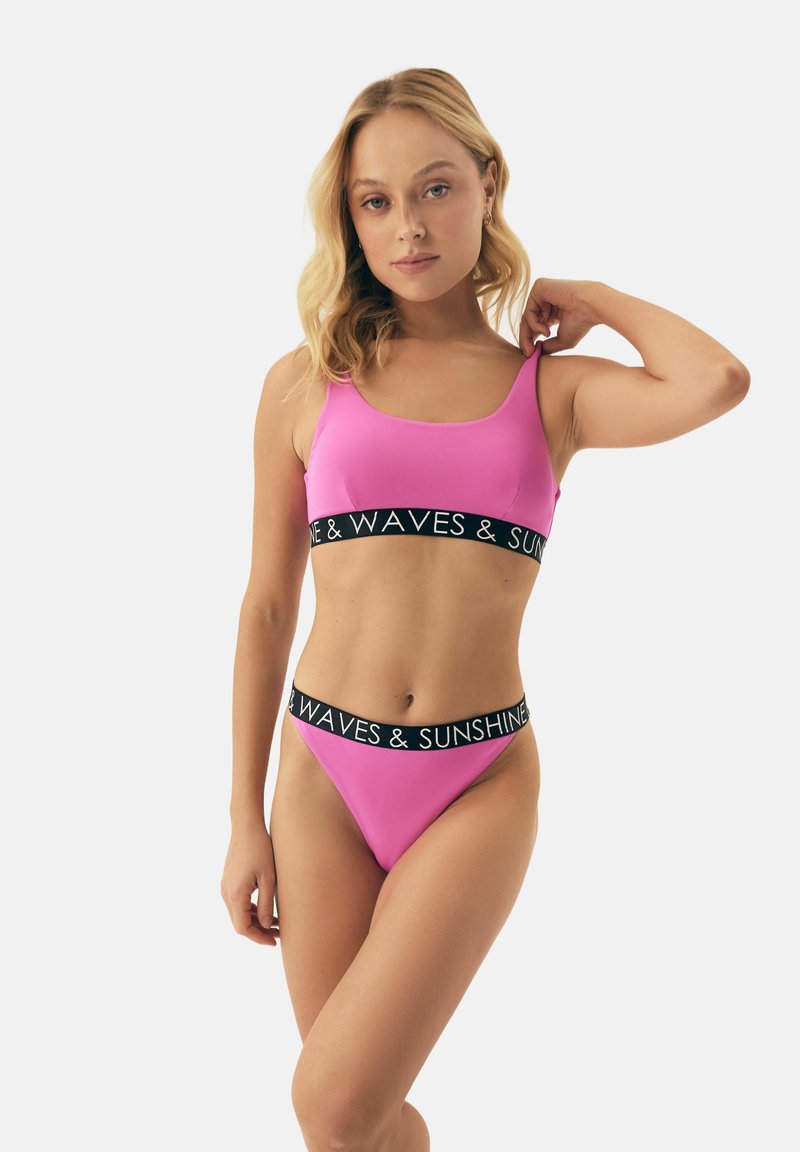 Różowy zestaw bikini z topem na szerokich ramiączkach i niskimi majtkami, oba z czarnym pasem z napisem "WAVES & SUNSHINE" w białym kolorze.