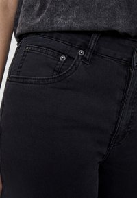 Pantalones vaqueros de mezclilla negra con un ajuste entallado, que cuentan con un diseño clásico de 5 bolsillos, acentos de metal y una ligera textura en la tela.