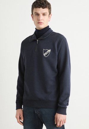 Navy sweatshirt with a half-zip collar, ribbed cuffs, and hem. Features an embroidered shield logo on the chest. Cotton blend fabric.