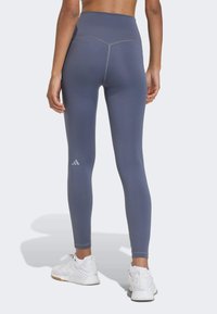 Grijze atletische legging met een hoge tailleband en versterkte naden, met een klein wit logo vlakbij de kuit. Gladde, rekbare stof.
