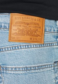 Los jeans de denim Levi's 511 presentan un lavado azul claro, una etiqueta de cuero con el logotipo en relieve y costuras en color cobre. Indicado tamaño W31 L32.